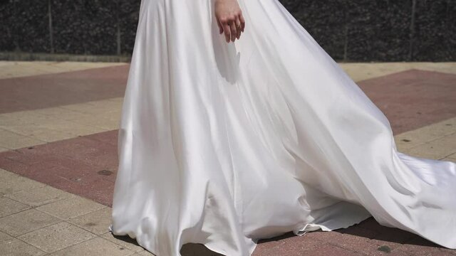 Bride in beautiful long white dress walks down the street in sunny weather in slow motion