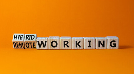 Hybrid or remote working symbol. Turned wooden cubes and changed words 'remote working' to 'hybrid working'. Beautiful orange background. Business, hybrid or remote working concept, copy space.