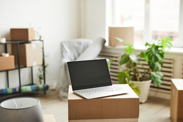 Background image of opened laptop with blank screen on cardboard boxes in new home, moving and relocation concept, copy space