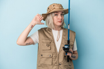 Young caucasian fisherwoman holding a rod isolated on blue background feels proud and self confident, example to follow.
