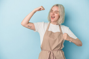 Young caucasian store clerk woman isolated on blue background raising fist after a victory, winner...