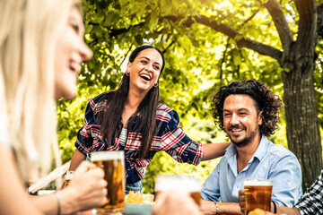 Happy friends celebrating drinking beer pint at park outdoor - Young people talking and laughing together at brewery pub garden - Friendship, youth and beverage concept