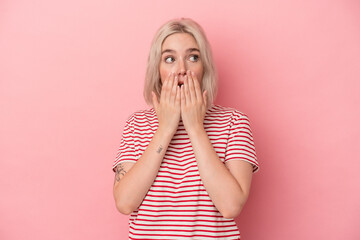 Young caucasian woman isolated on pink background thoughtful looking to a copy space covering mouth with hand.