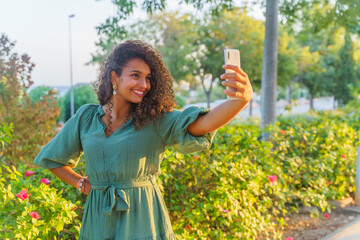 Curly haired Hispanic woman on the street while she is happy and takes a selfie with a smartphone