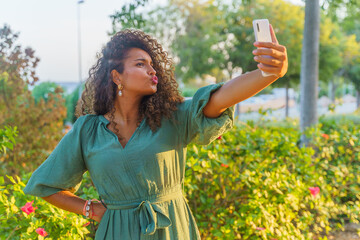Curly haired Hispanic woman on the street making funny faces and taking a selfie with smartphone