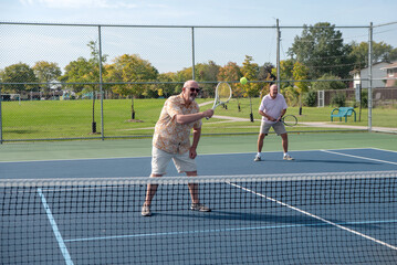 Obraz premium Active gay seniors play tennis in an outdoor court on a sunny day.