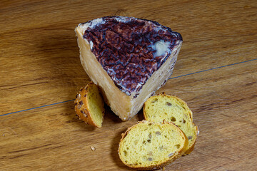 Closeup of a triangular portion of pyrenean cheese with three slices of turmeric bread with seeds on a light colored wooden background