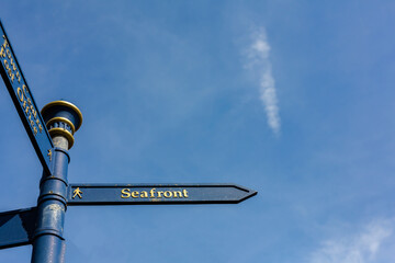 Public information sign showing the direction to the sea front, isolated against a clear blue summer sky