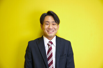 黄色い背景の前で爽やかに笑うスーツを着た日本人男性
