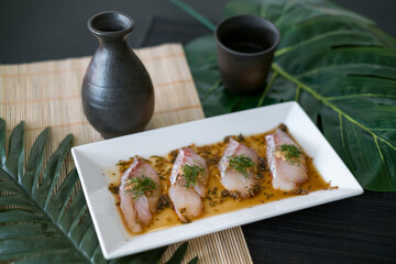 Sea bass sashimi with sauce on white plate, black decanter with sake and glass on the table. Japanese restaurant. Japanese traditional food. Raw fish 