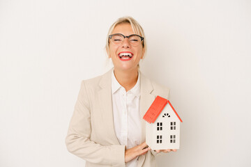 Young real estate agent woman holding a home model isolated on white background laughing and having...