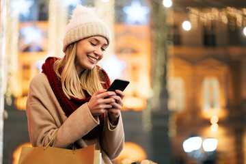 Portrait of young smiling beautiful woman using smartphone on the street at winter - Powered by Adobe