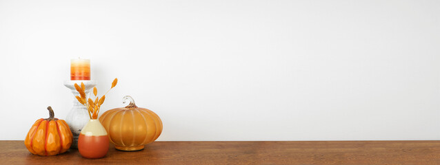 Autumn decor on a wood shelf against a white wall banner background. Pumpkins, candle and vase with...