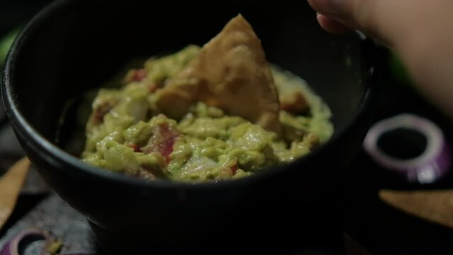 Hand dipping tortilla chip in bowl of guacamole surrounded by tortilla chips