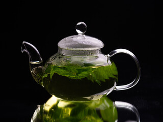 Hot glass teapot on a black background, green mint tea. Herbal tea and healthy drink concept.