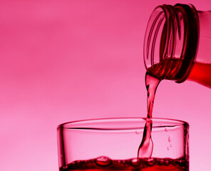 A red drink is poured into a transparent glass from a bottle.