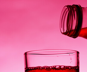 A red drink is poured into a transparent glass from a bottle.