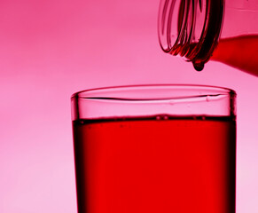 A red drink is poured into a transparent glass from a bottle.