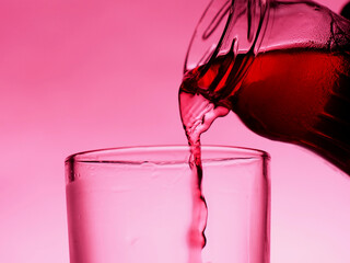 A red drink is poured into a transparent glass from a bottle.