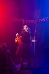Little girl holds broom on Halloween holiday. Kid girl wear witch costume. Fantasy, fairy tale and masquerade concept.