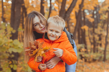 Mother hugging her child during walk in autumn park. Fall season and single parent concept.