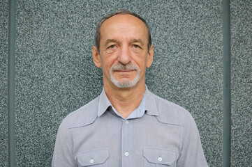 Male portrait of older coworker in blue shirt near dark grey wall