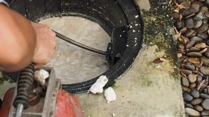 Drain cleaning. Plumber repairing clogged grease trap with auger machine. Maintenance the sewage...