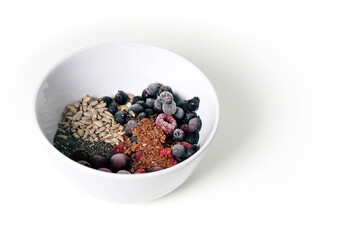 Fototapeta na wymiar Healthy breakfast in a plate. Chia seeds, flax, sunflower seeds, nuts, frozen berries: irga, cherry and raspberry in a white plate on a white isolated background. Vegan foo
