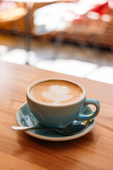 One Cup of cappuccino with latte art. Coffee in blue cup on wooden table in cafe. Concept of easy breakfast.
