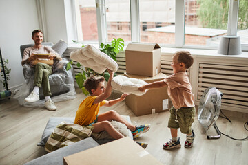 Side view portrait of two brothers enjoying pillow fight in room with boxes while family moving in...