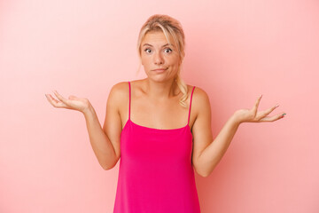 Young Russian woman isolated on pink background doubting and shrugging shoulders in questioning...