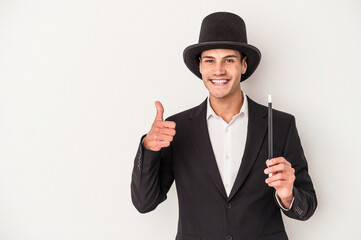 Young magician caucasian man holding a wand isolated on white background smiling and raising thumb up