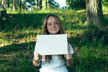 Teen girl holding clean white sheet paper (for your message), in the park.
