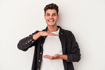 Naklejka premium Young caucasian man isolated on white background holding something with both hands, product presentation.