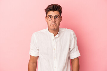 Young caucasian man isolated on pink background shrugs shoulders and open eyes confused.