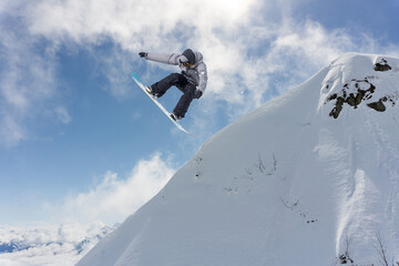 A jumping snowboarder in the mountains. Snowboarding, winter extreme sport.