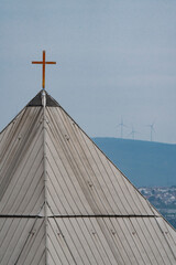 a golden cross on the roof of a pyramid like architecture church witch chills and forest in the background