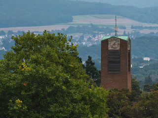 a church tower between trees and the city, hills and forest in the background 