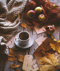 A cup of coffee stands on a wooden background, apples and autumn leaves are on the table.