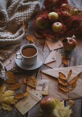 A cup of coffee stands on a wooden background, apples and autumn leaves are on the table.