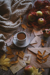 A cup of coffee stands on a wooden background, apples and autumn leaves are on the table.