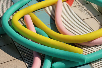 Multi-colored poolside noodles lit by the sun. The noodles are floating tubes in expanded resin for water aerobics and for pool fun.