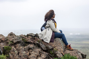 mixed race African American  woman is sitting on a mountain  edge enjoying the inspiring view from the top. the black woman is enjoying her freedom to explore the Iceland adventure