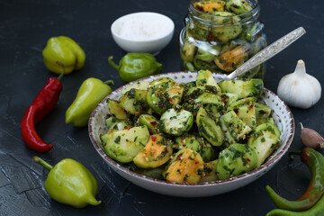 Salad of green tomatoes with pepper, garlic, dill and parsley on a dark gray background