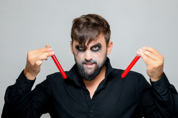a bearded man with undead makeup for Halloween holds test tubes in which red liquid
