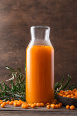Sea buckthorn juice in glass jug and fresh autumn berries on wooden background. Healthy antioxidant...