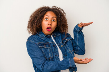 Young african american woman with curly hair isolated on white background shocked and amazed holding a copy space between hands.