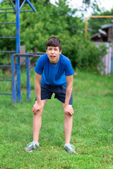 teenage boy exercising outdoors, sports ground in the yard, he posing and does a warm-up, healthy lifestyle