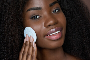 Pretty African ethnic black young woman holding cotton pad removing face make up with makeup...