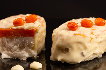 Eskimo cheese cake with buckthorn and white chocolate icing on black background 